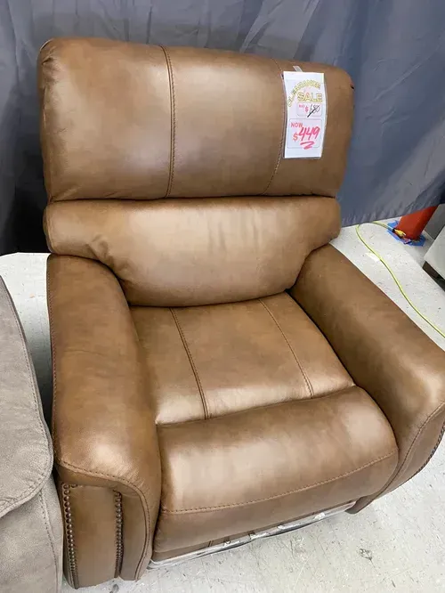 Brown leather recliner chair with tag, indoor setting.