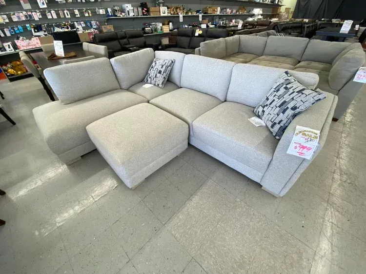 Light-colored sectional sofa with ottoman and two decorative pillows in a store setting.