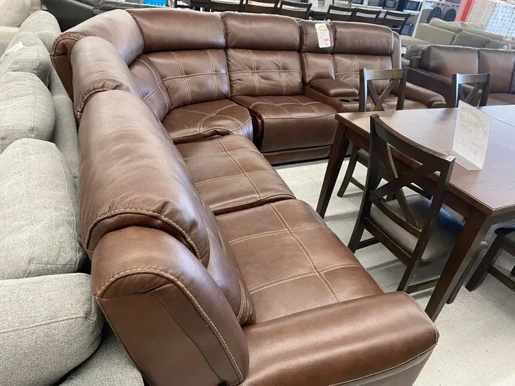 Brown leather sectional sofa next to a dark wood dining set in a furniture store.