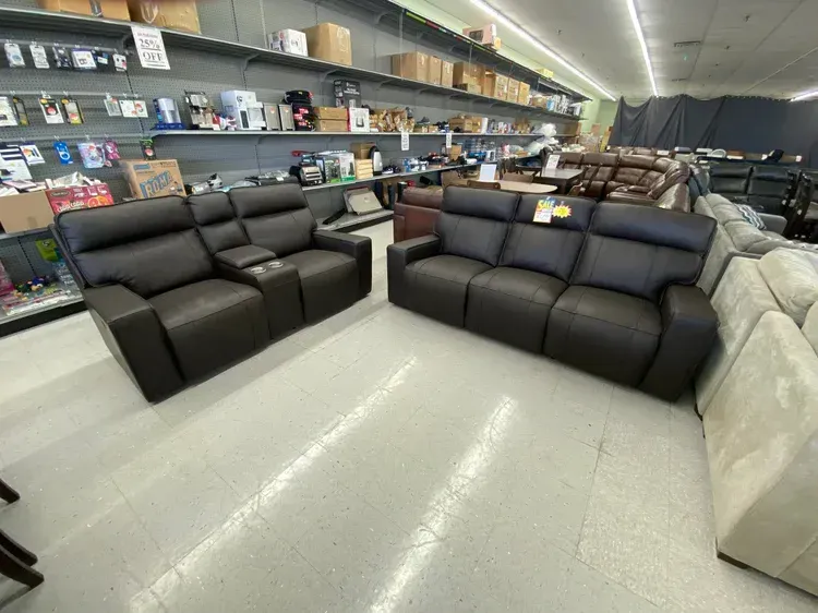 Two black leather reclining sofas in a furniture store, angled view.