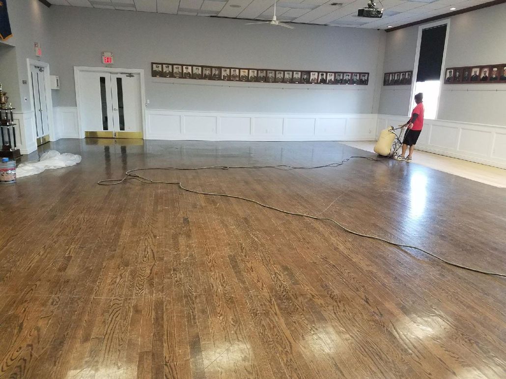 Empty hall with worn wooden floor, white walls, and a person standing near the right wall.