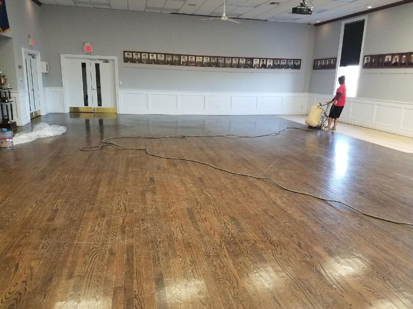Empty hall with worn wooden floor, white walls, and a person standing near the right wall.