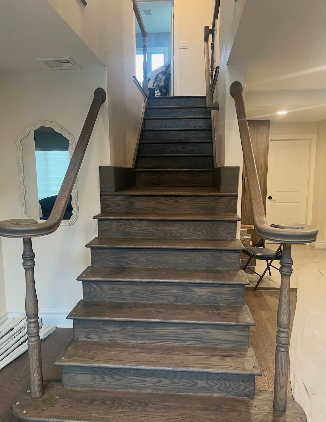 Indoor staircase with wooden steps, dark handrails, and white walls leading to an upstairs hallway