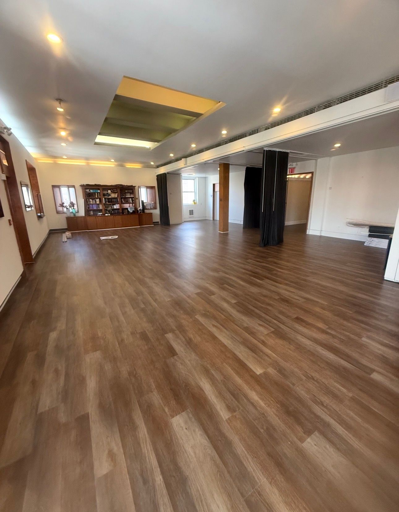 Empty modern hall with wood floors, recessed ceiling lights, and a large open layout.