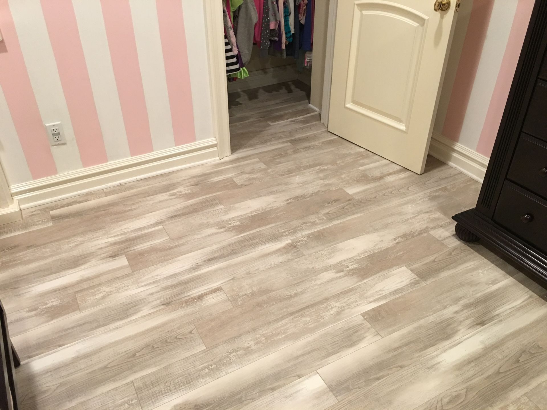 Empty bedroom with light wood flooring, pink striped walls, and an open closet door.