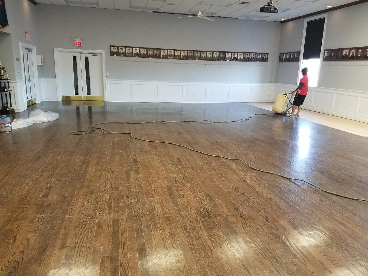 Empty community hall with wooden floor, white walls, and a person near the right wall