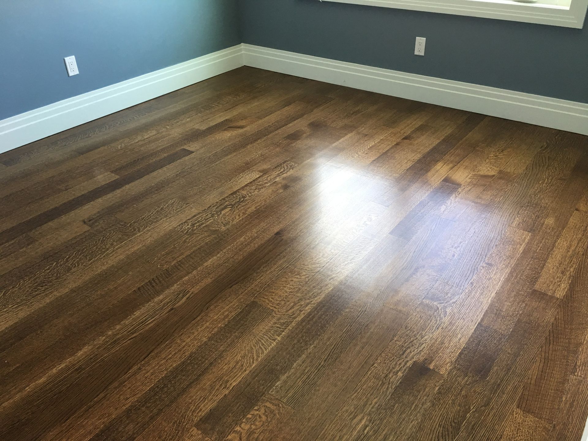 Empty room with dark wood floors, gray walls, white baseboards, and sunlight reflecting on the floor