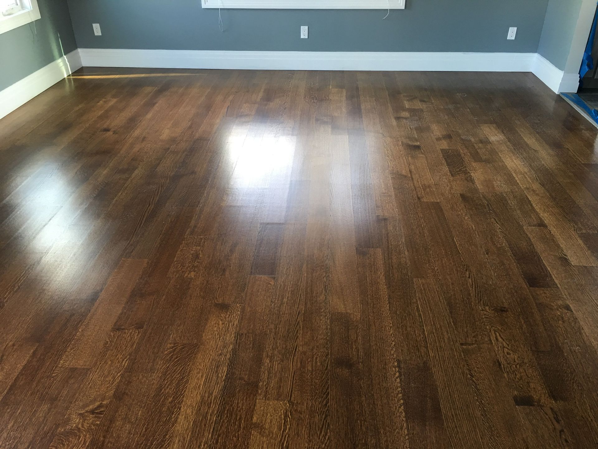 Empty room with dark hardwood floors and gray walls, lit by sunlight from windows.