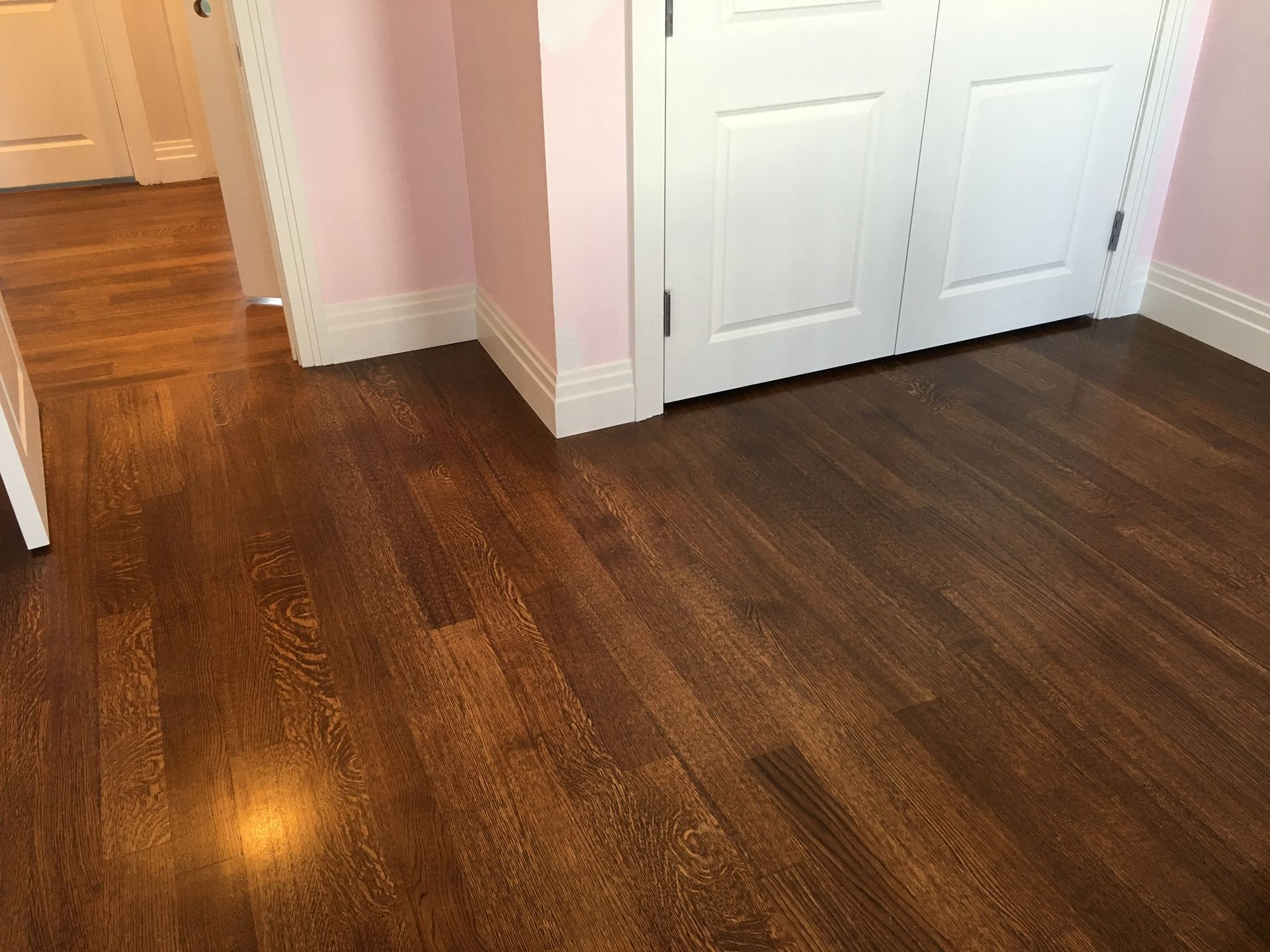 Dark hardwood floor in a hallway with white double doors and light pink walls.