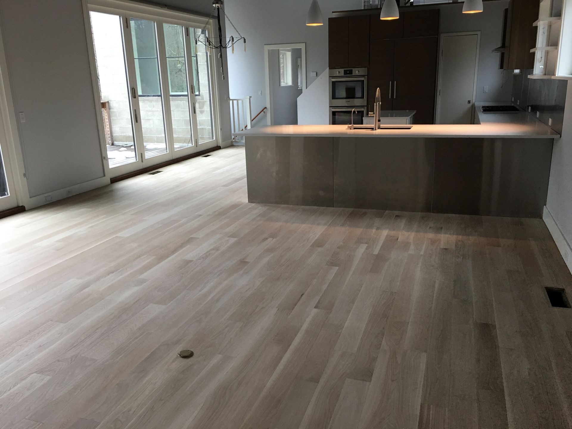 Empty modern kitchen and living area with light wood floors, island, and sliding glass doors.
