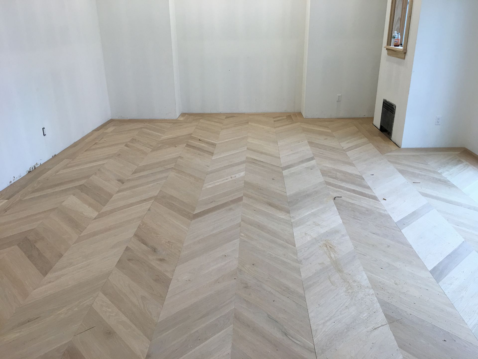 Empty light-filled room with pale herringbone wood floor and white walls