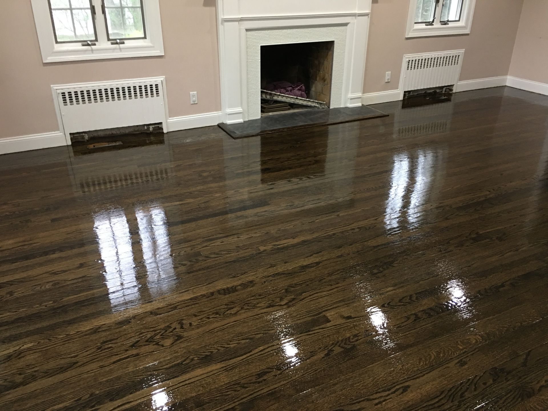 Polished dark hardwood floor in a living room with a fireplace and windows reflecting light.