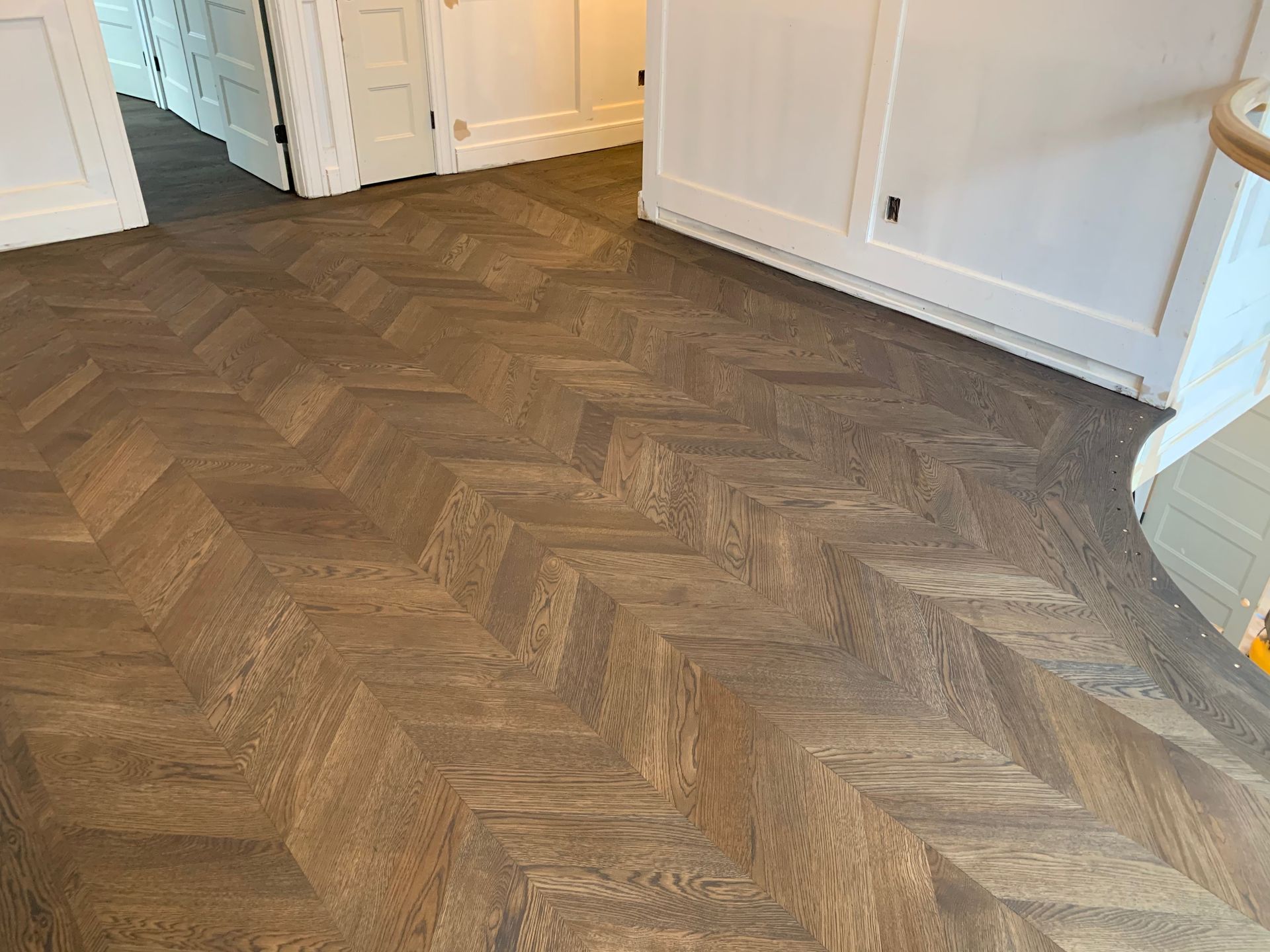 Patterned wood herringbone floor in a bright hallway with white cabinets and doors