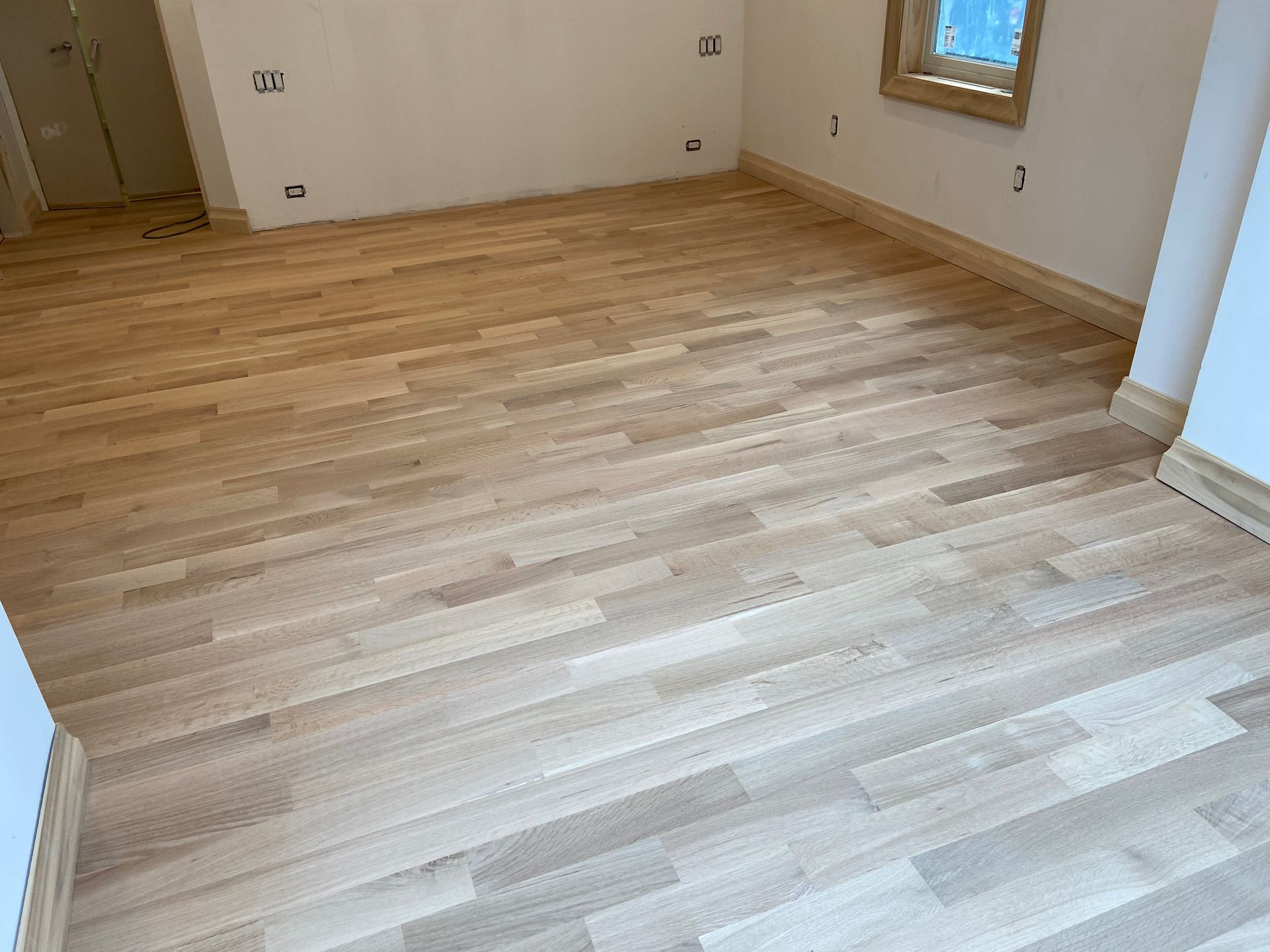 Empty hardwood-floored room with white walls and a window.