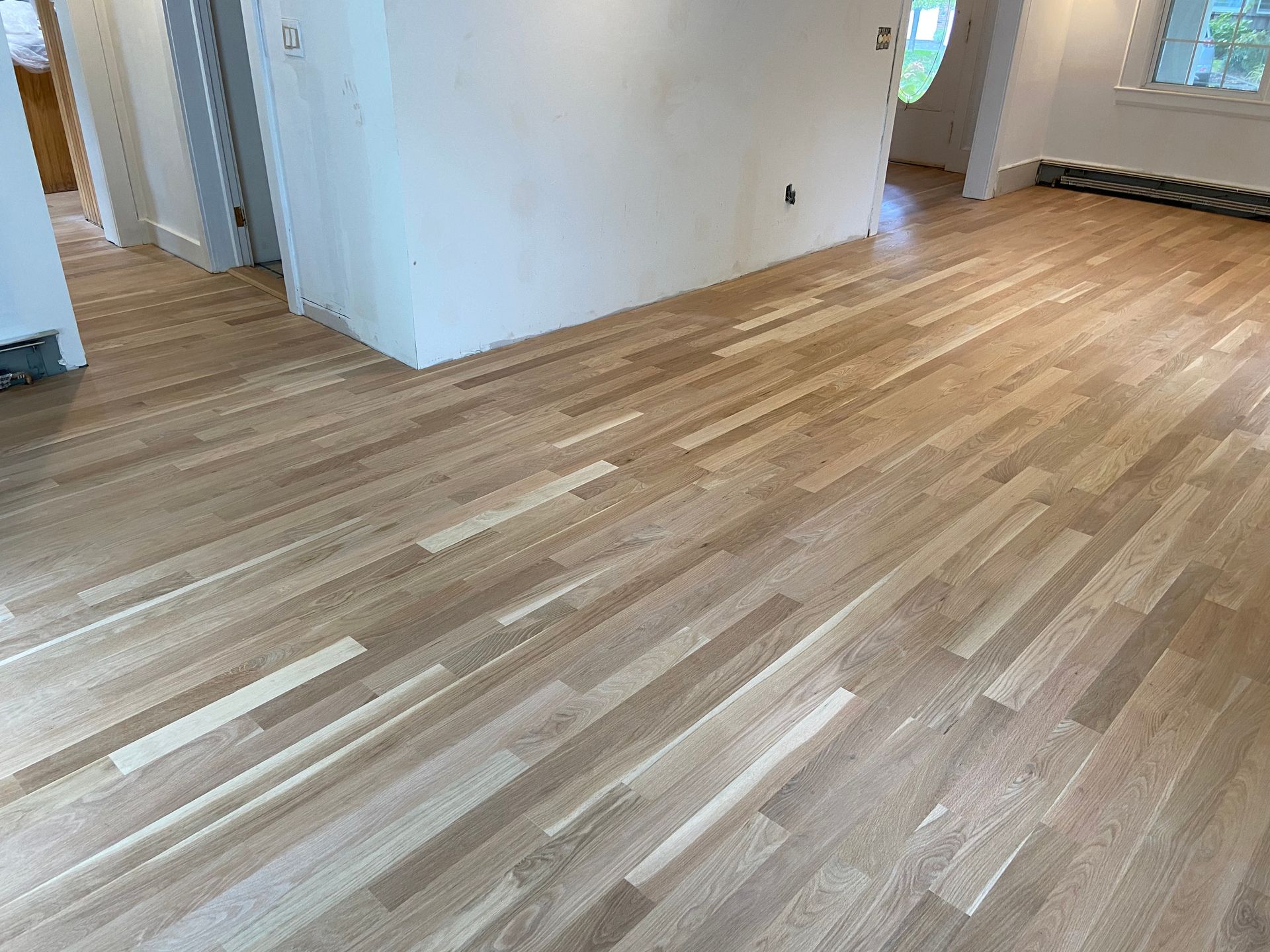 Empty room with light wood flooring and white walls, viewed from a corner near a doorway.