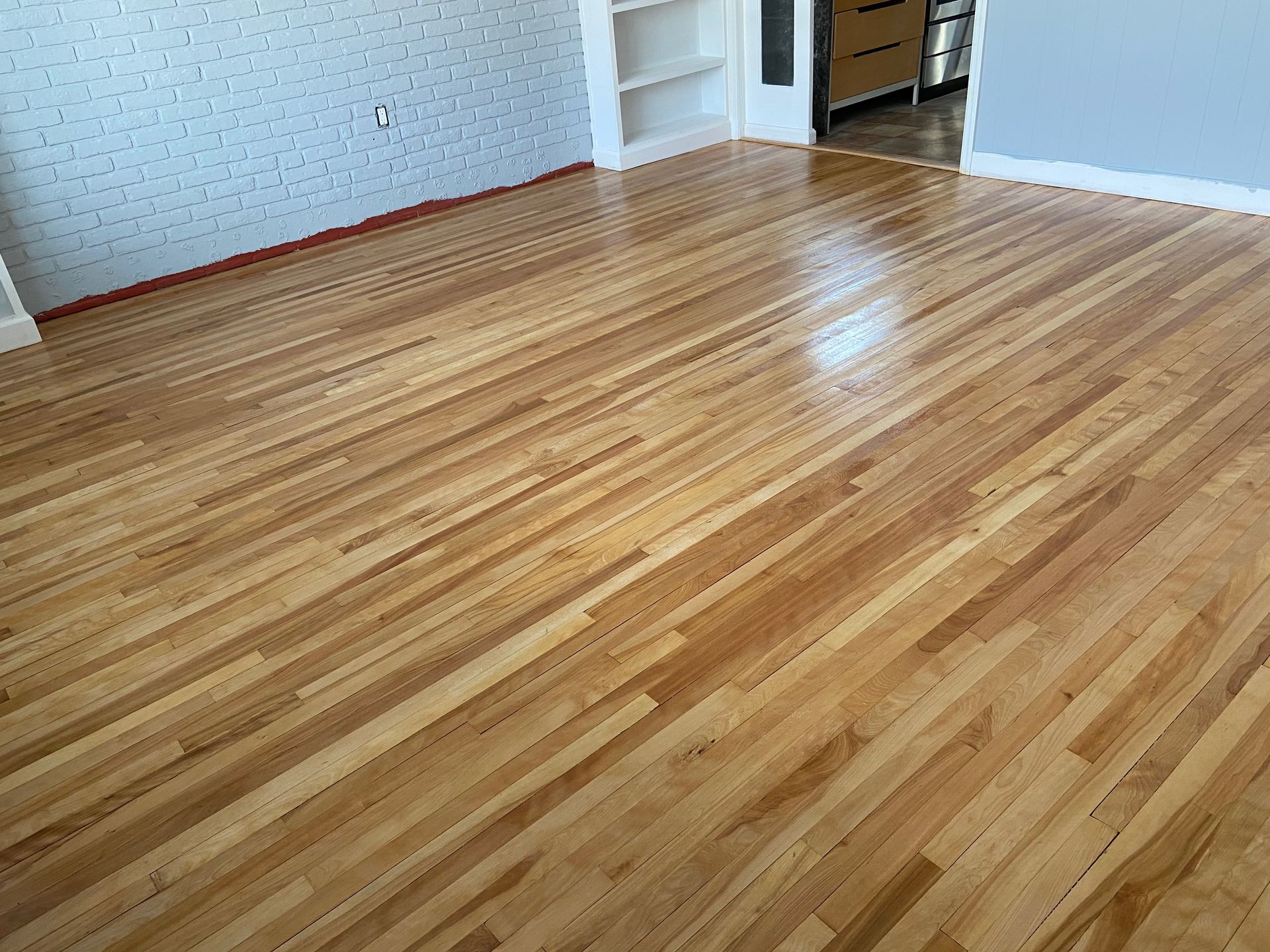 Empty room with polished hardwood floors and white walls, viewed toward an open doorway.