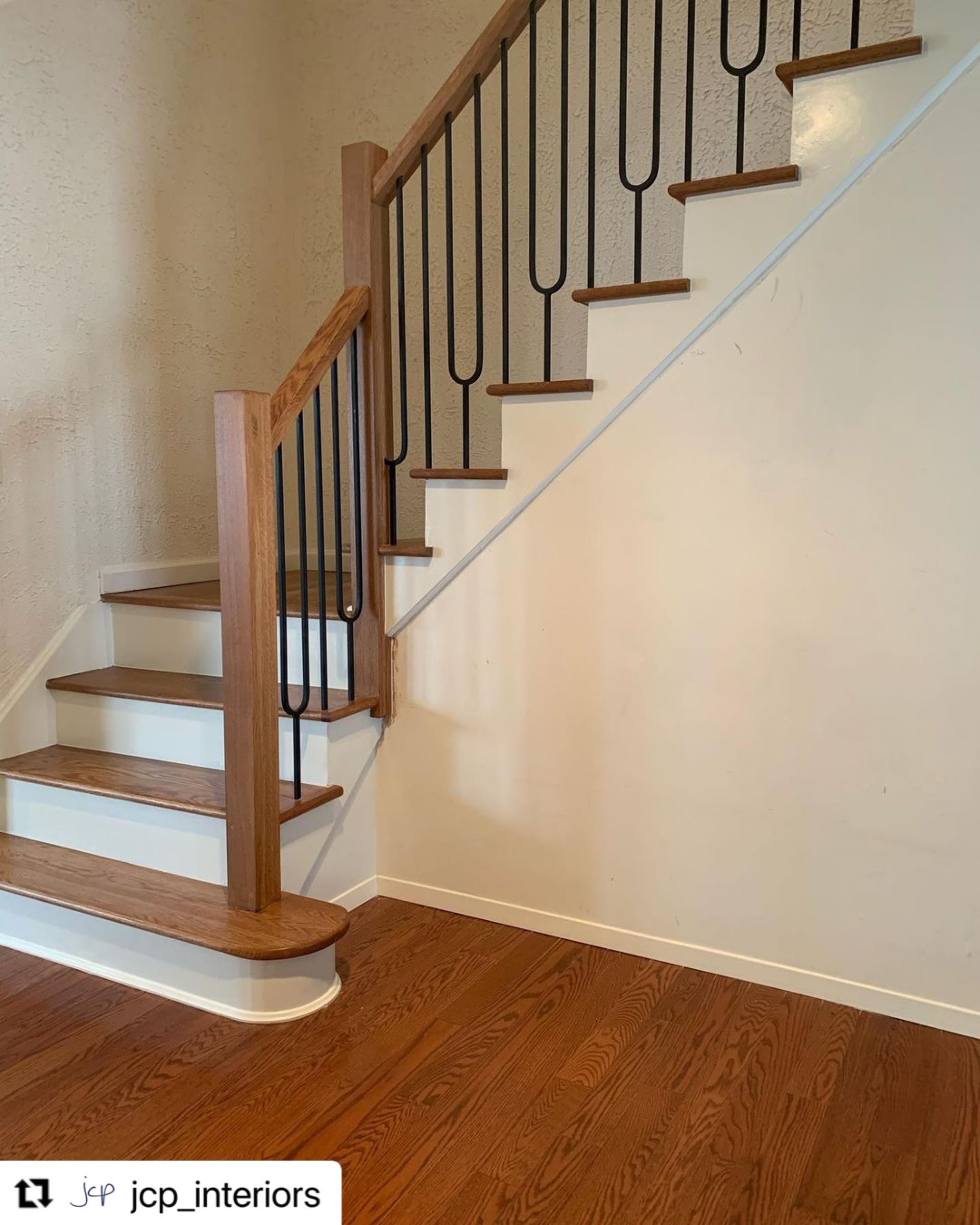 Staircase with wood steps, white risers, and dark iron railing in a home interior.