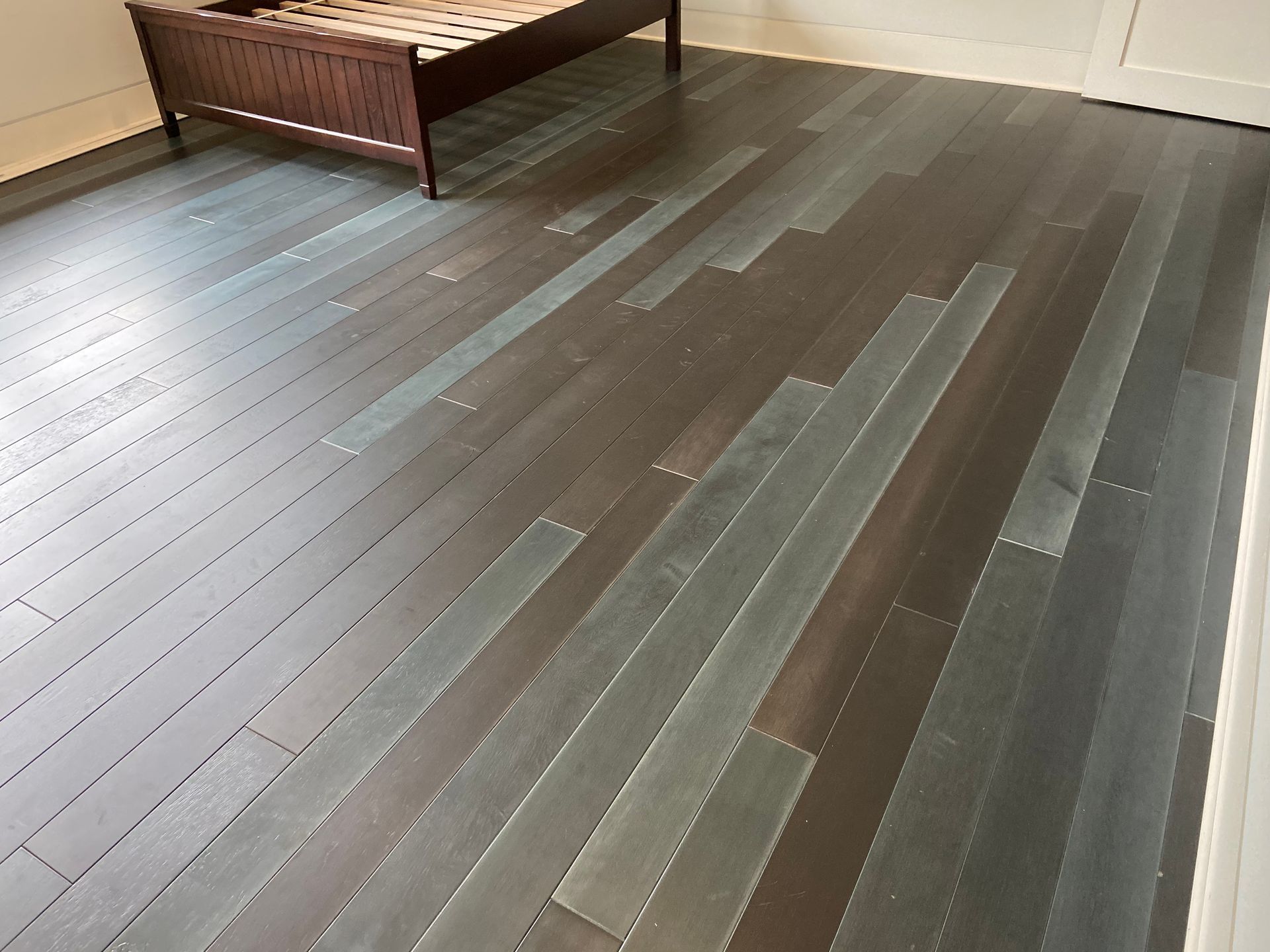 Dark wood floor with long gray inlaid planks beside a wooden bench in a room.