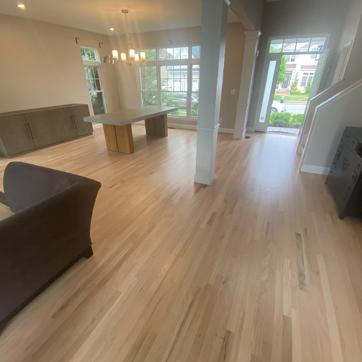 Bright open living room with light wood floors, large windows, a kitchen island, and a sofa.