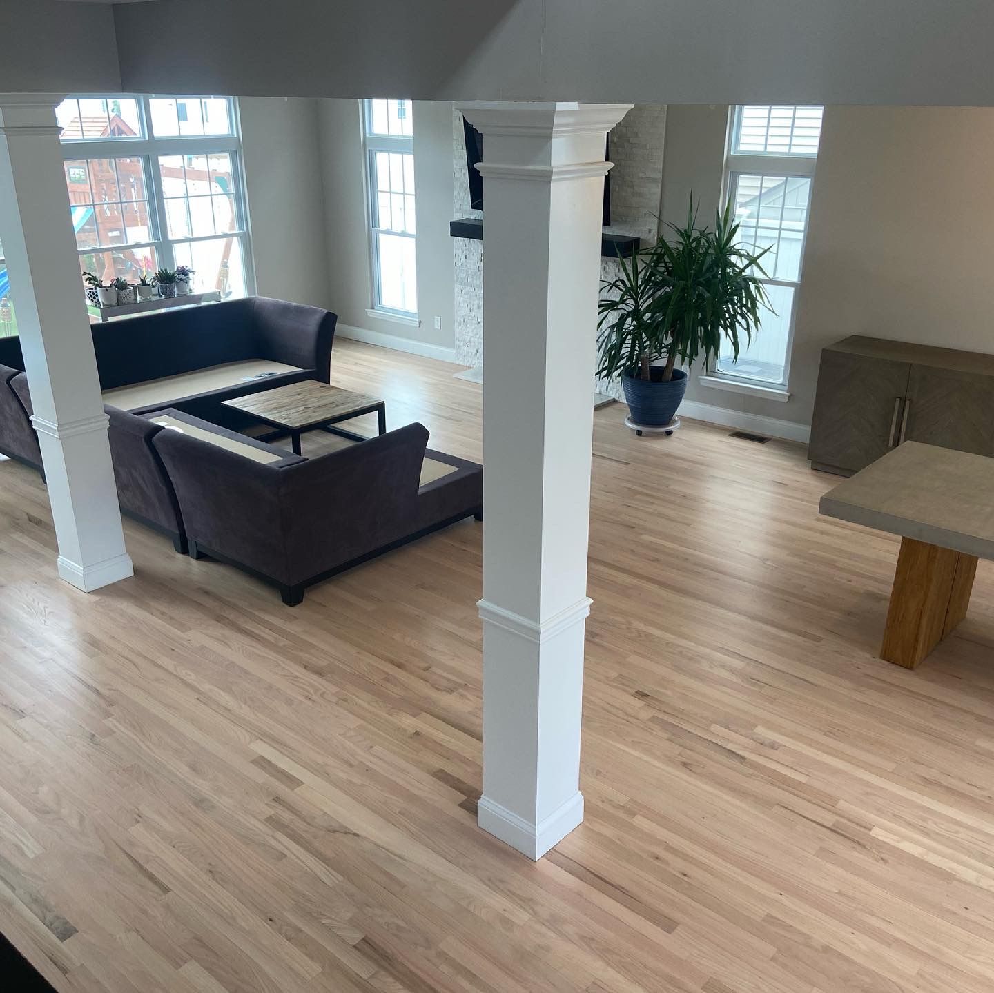 Empty modern living room with gray sofa, wood floor, white columns, and large windows
