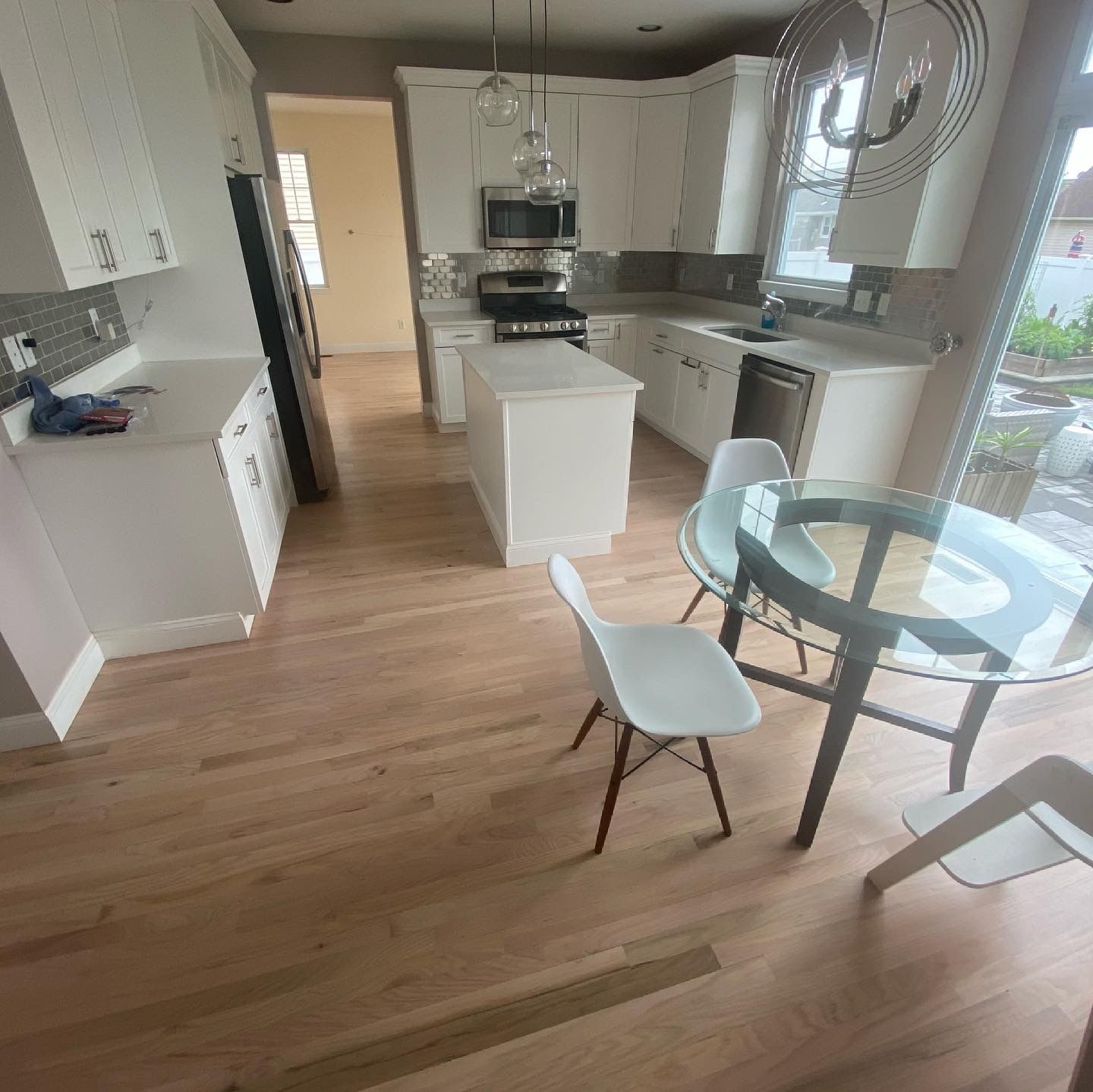Bright modern kitchen with white cabinets, island, and glass dining table beside a window.