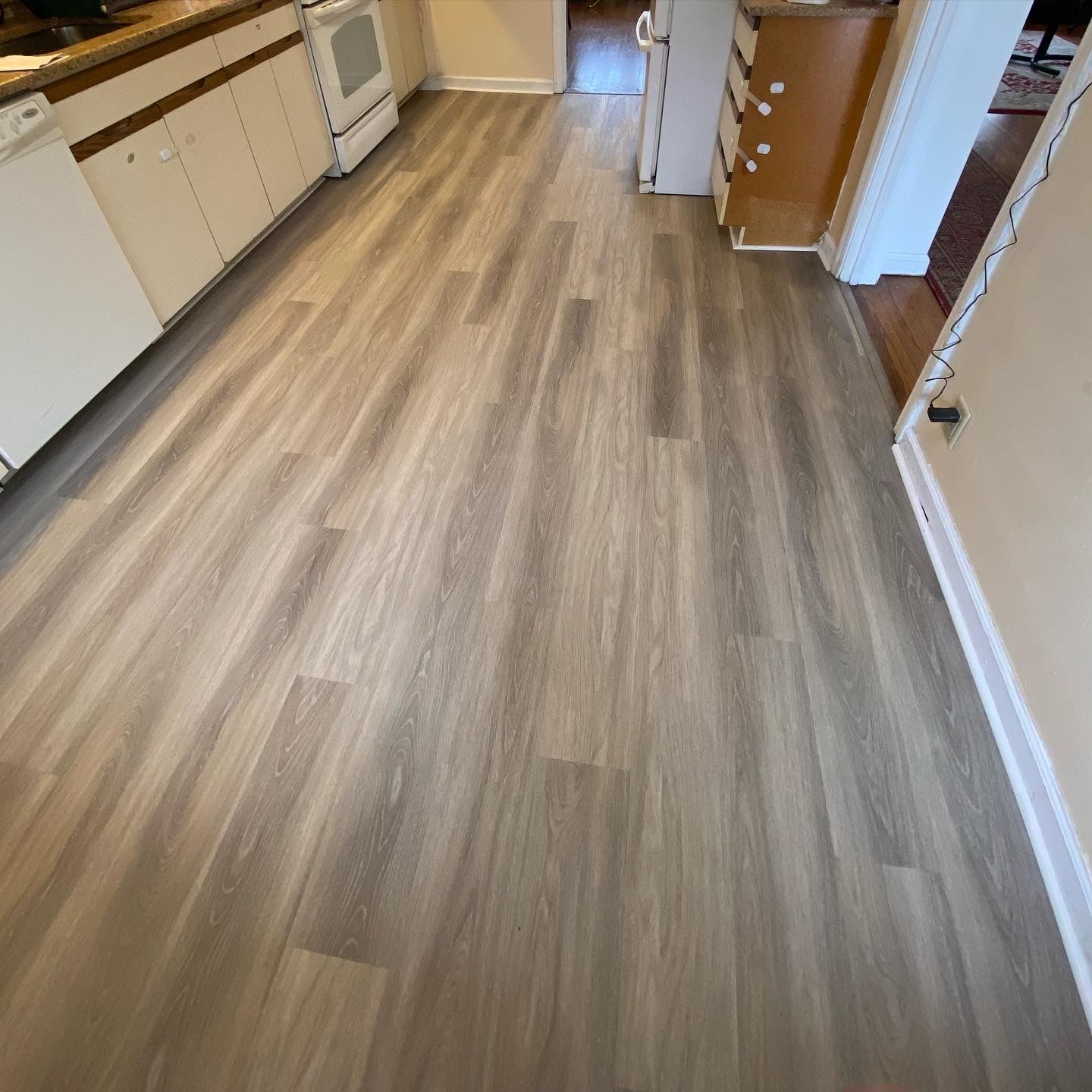Empty kitchen with wood-look flooring and white cabinets, viewed from a doorway