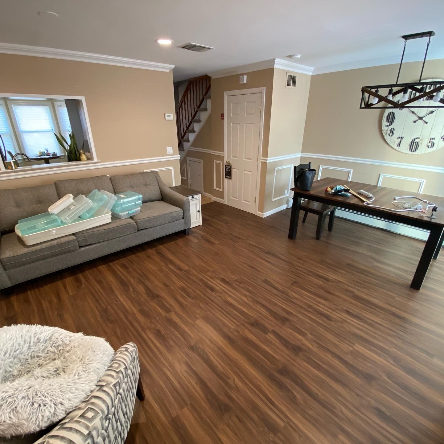 Bright living room with wood floors, gray sofas, glass dining table, and large wall clock