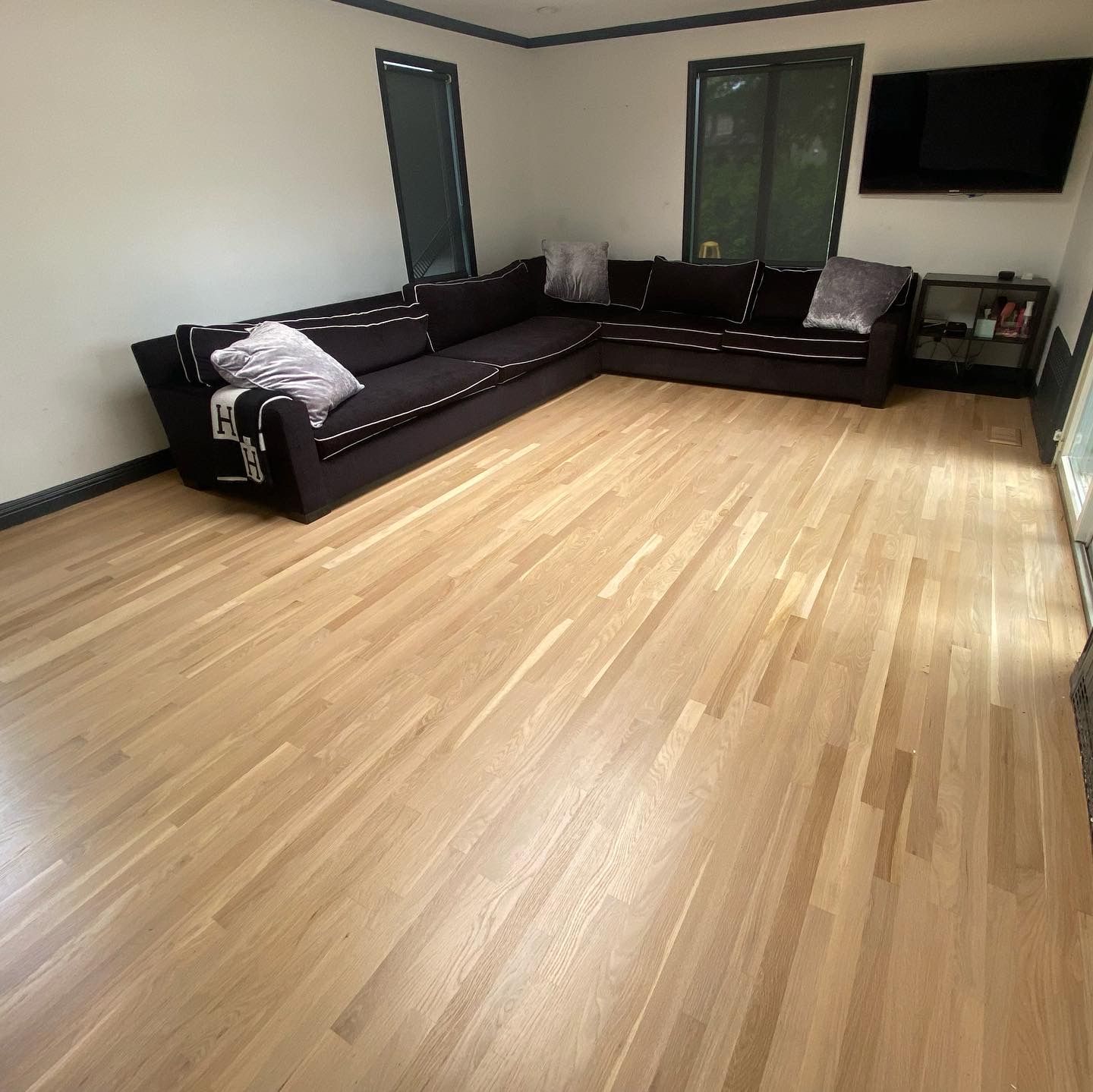 Modern living room with dark sectional sofa, light wood floor, and wall-mounted TV