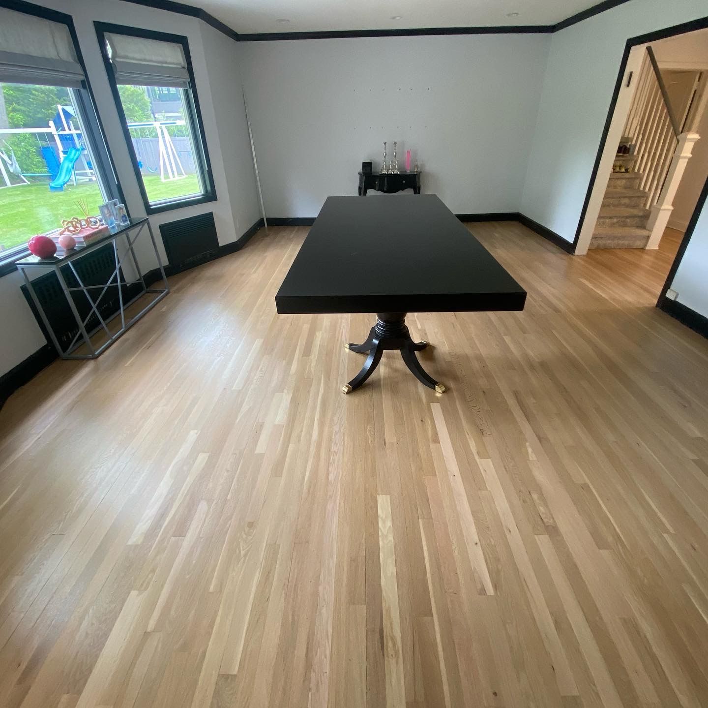 Bright room with a black table, wood floor, windows, and a staircase in the corner