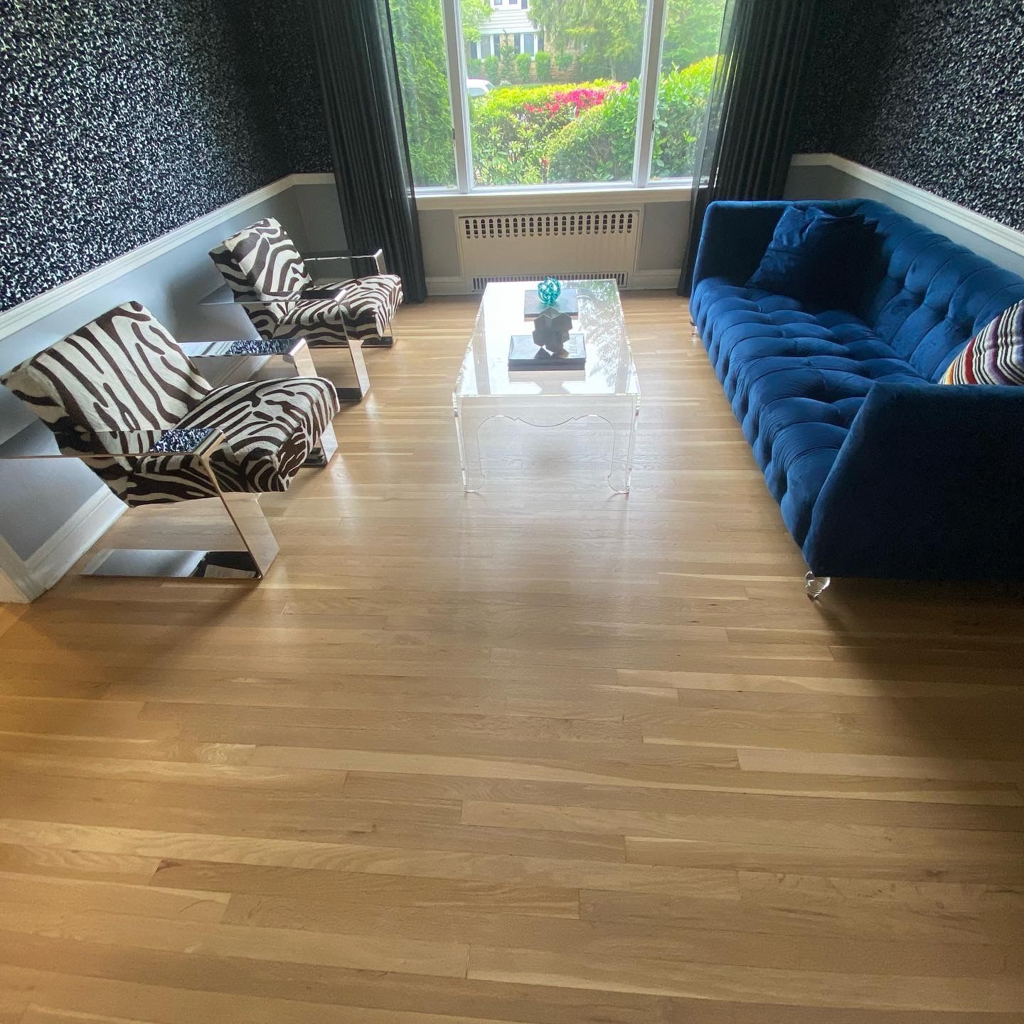 Modern living room with blue sofa, two zebra chairs, and a glass coffee table by a bright window.