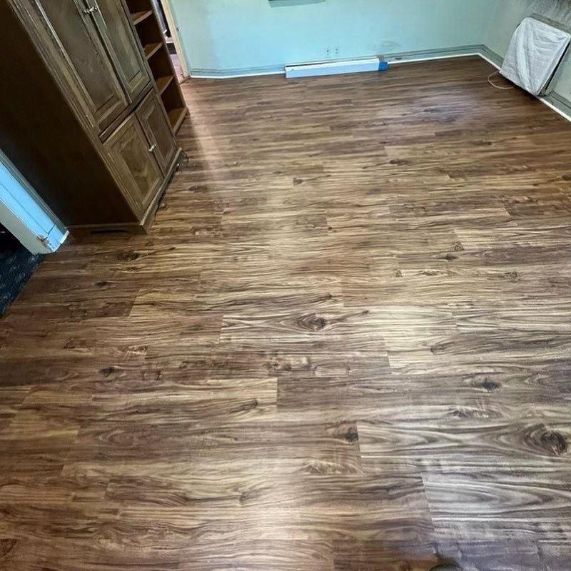 Empty room with wood-look flooring, a cabinet on the left, and a window with a white curtain on the right.