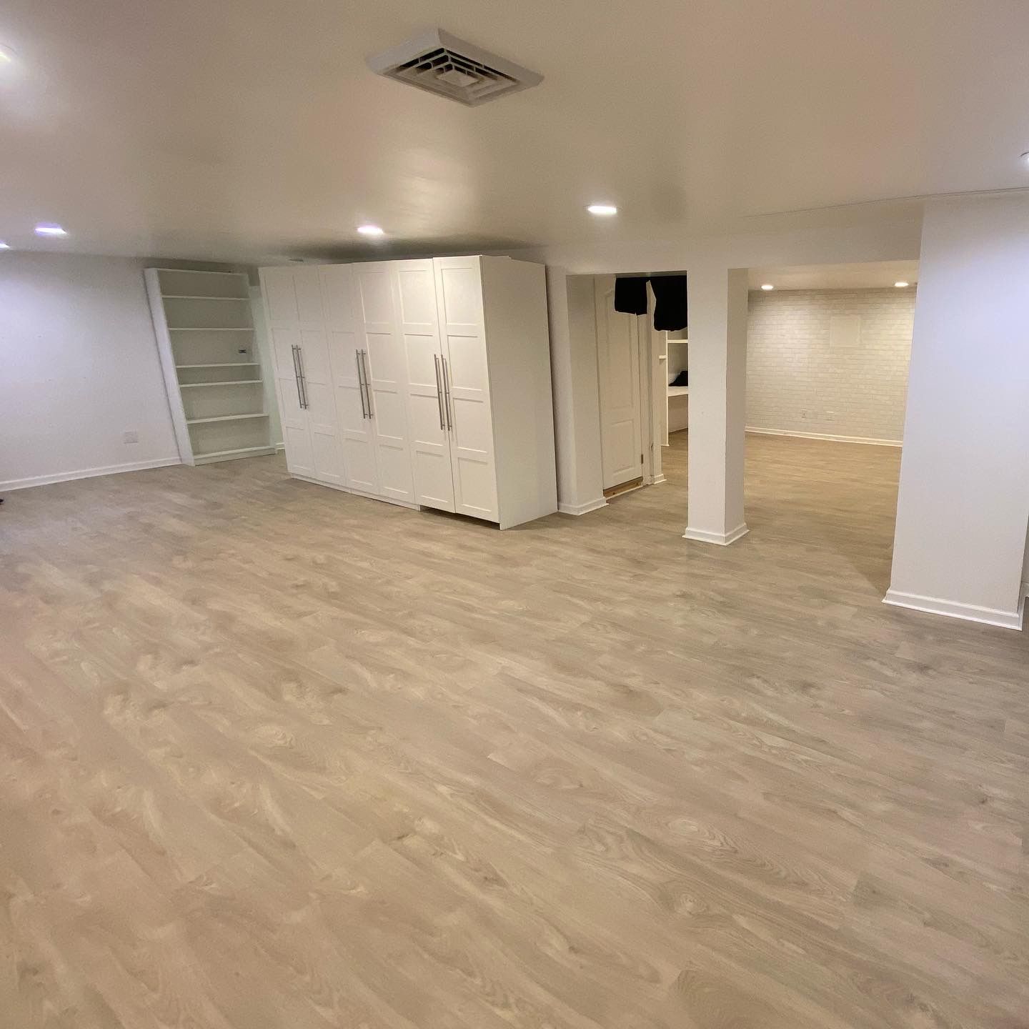 Empty basement room with light wood floor, white walls, and recessed ceiling lights