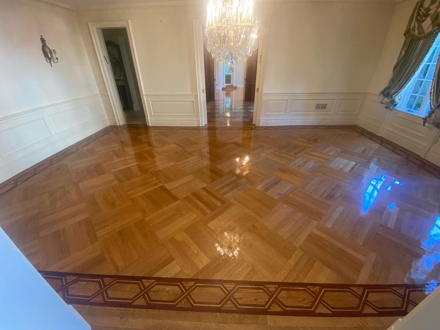 Empty formal room with polished parquet floor, chandelier, white walls, and blue drapes