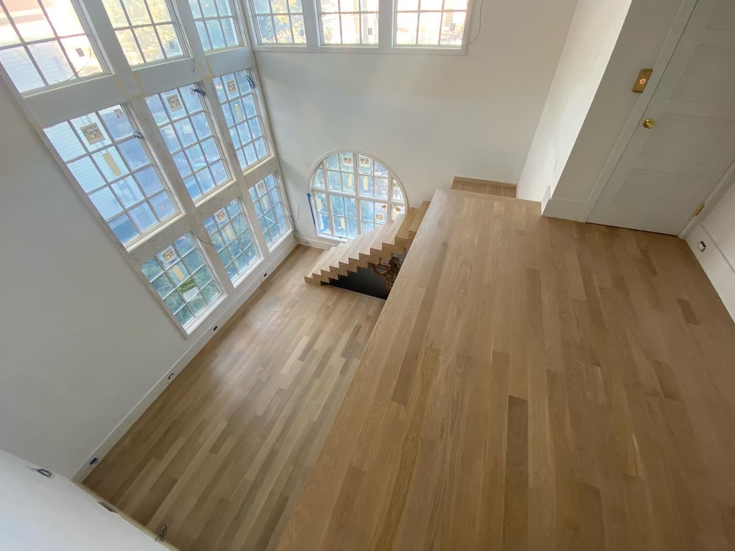 Bright loft interior with wood floors, large grid windows, and a staircase opening below