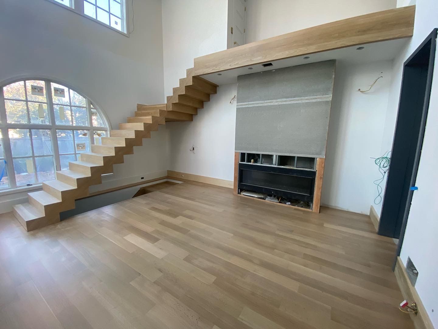 Bright modern loft with wooden stairs, large windows, and a fireplace on a light wood floor.