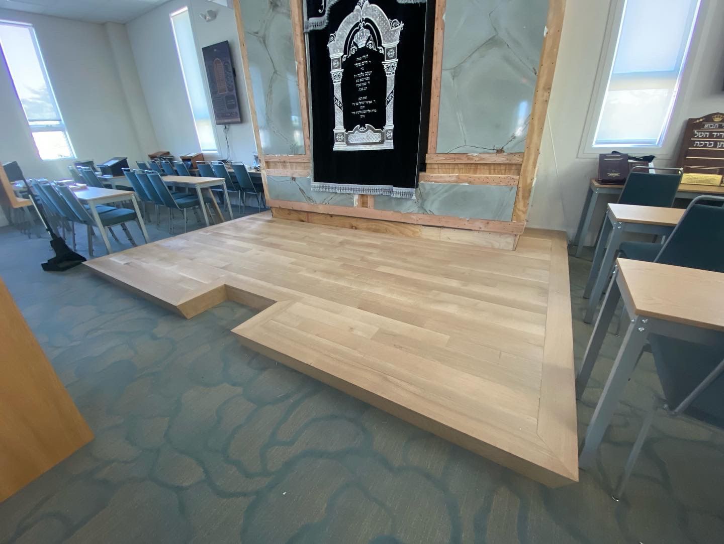Raised wooden stage in a classroom with blue chairs and tables around it