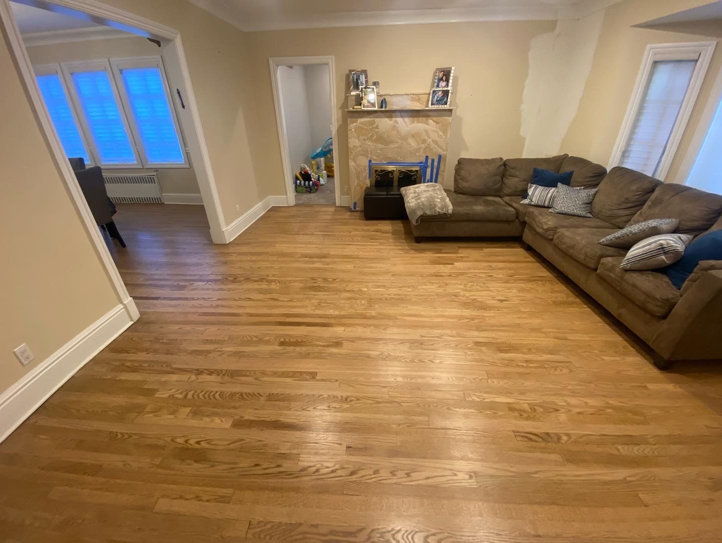 Spacious living room with hardwood floors, brown sectional sofa, fireplace, and windows with blue shades.