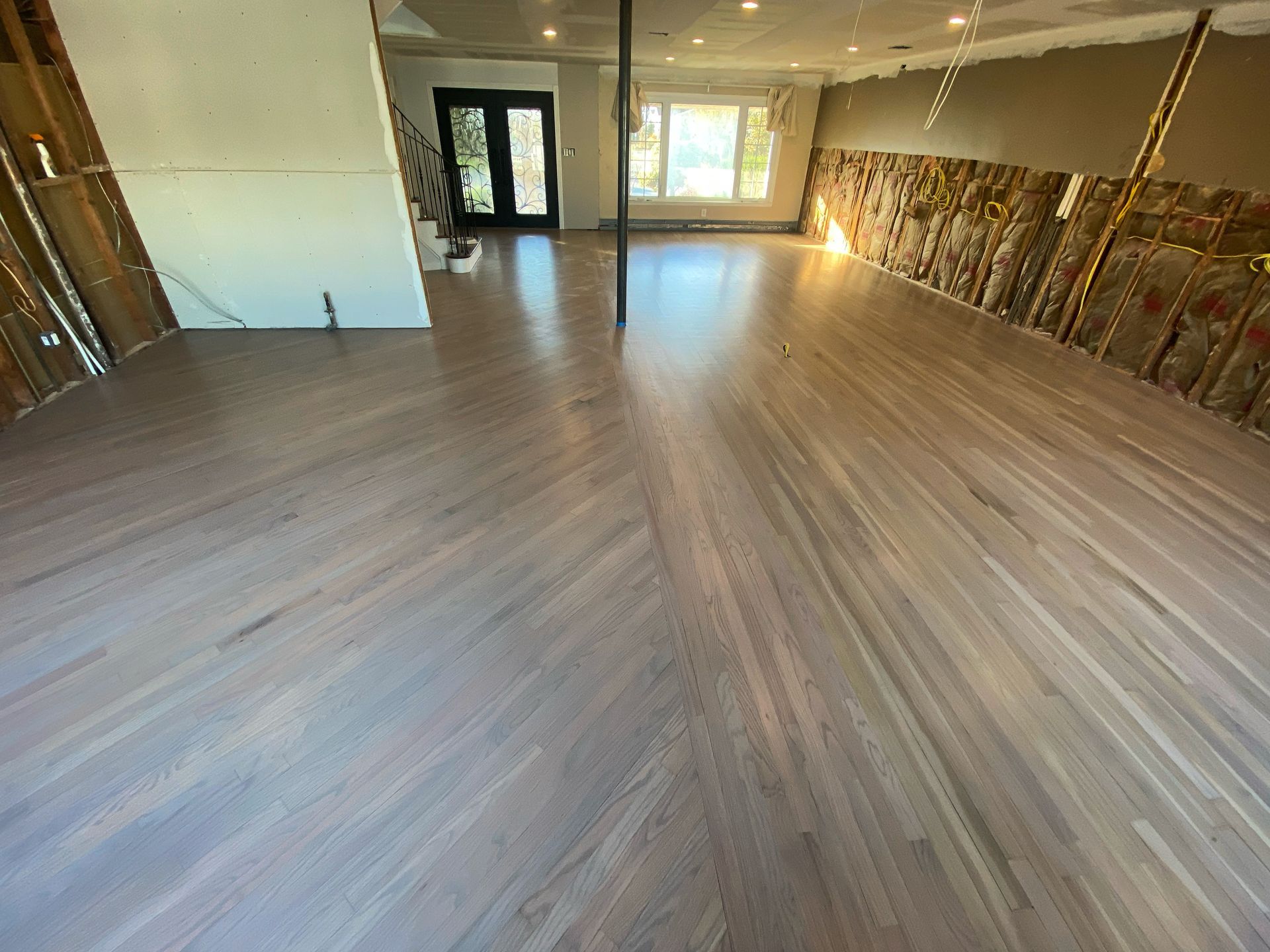 Empty room with light wood flooring, exposed walls, and large windows and glass doors at the back.