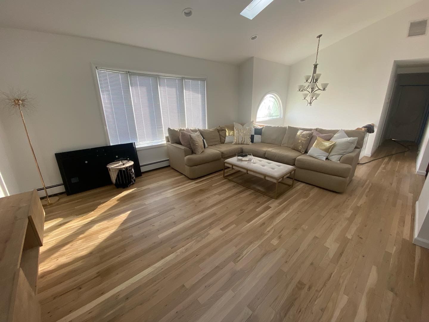 Bright living room with beige sectional sofa, coffee table, chandelier, and sunlight on hardwood floors