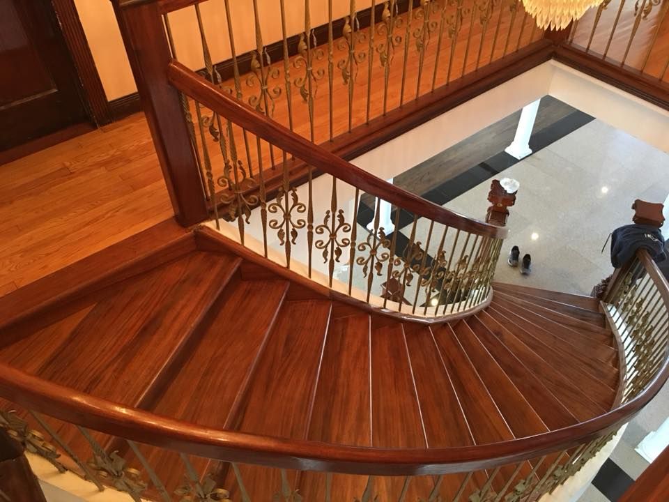 Curved wooden staircase with ornate railing viewed from above in a warm-lit interior