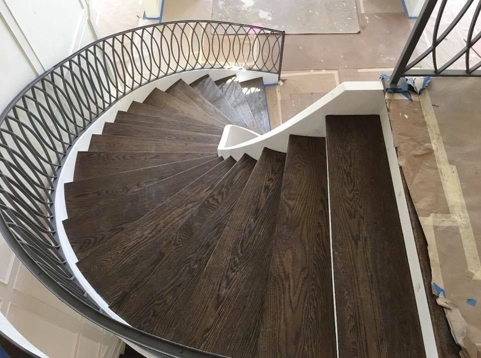 Curved dark wood staircase with decorative metal railing in a bright interior.