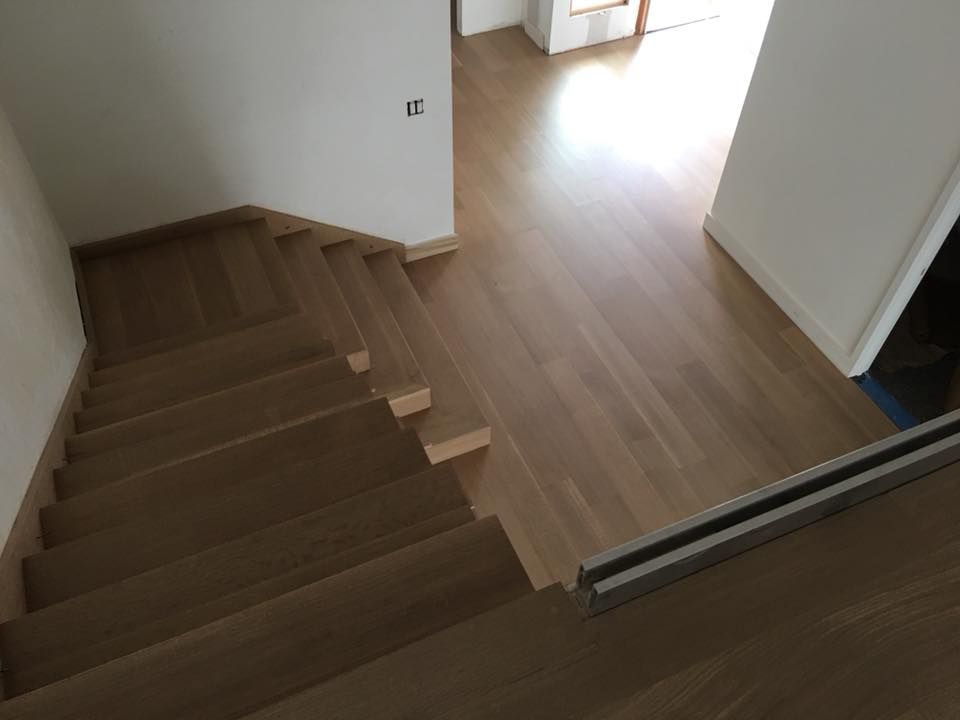 Wooden staircase leading to a bright hallway with light wood flooring and white walls