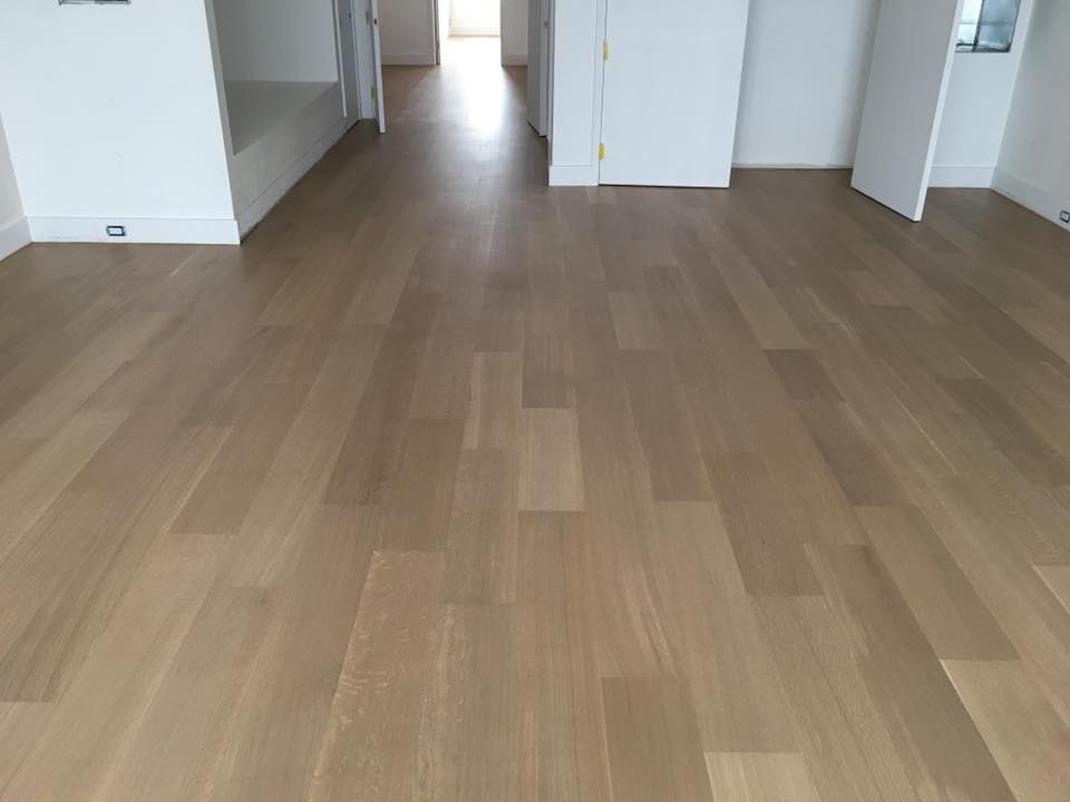 Empty room with light wood flooring and white walls, viewed from a doorway corridor.