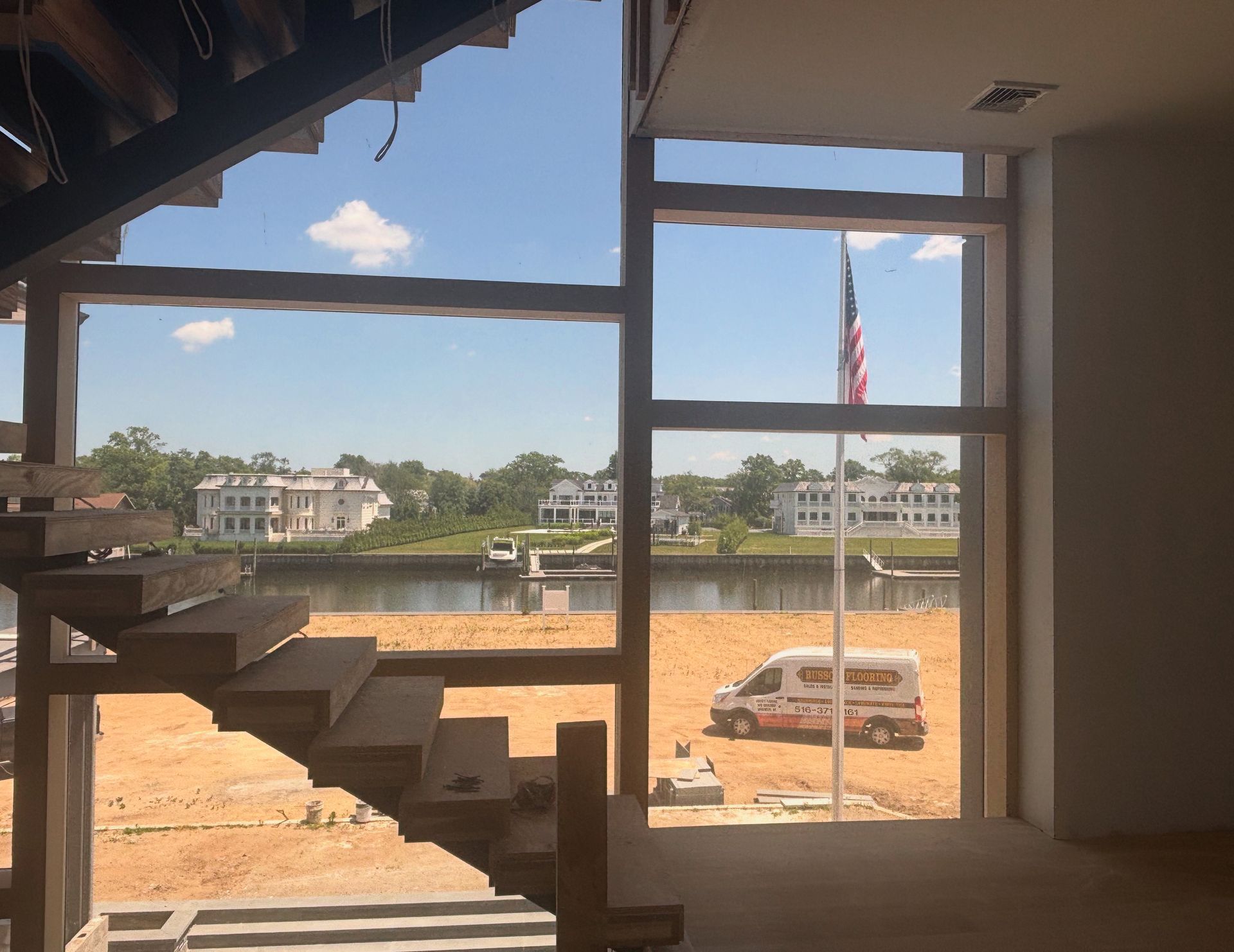 Interior view through window frame onto a construction site with dirt lot, van, and flagpole.