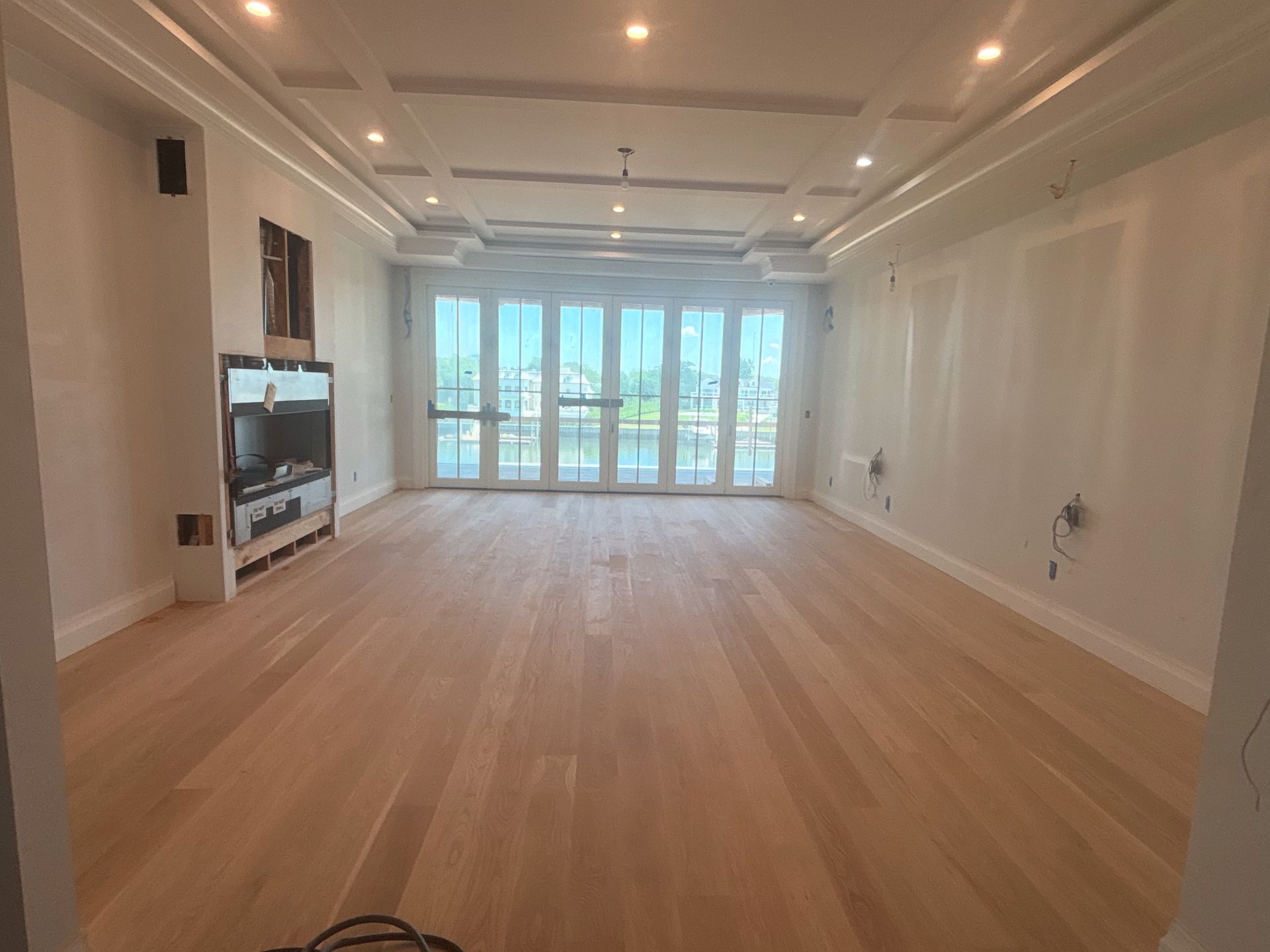 Empty modern living room with light wood floors, recessed lights, and large glass doors to a balcony.