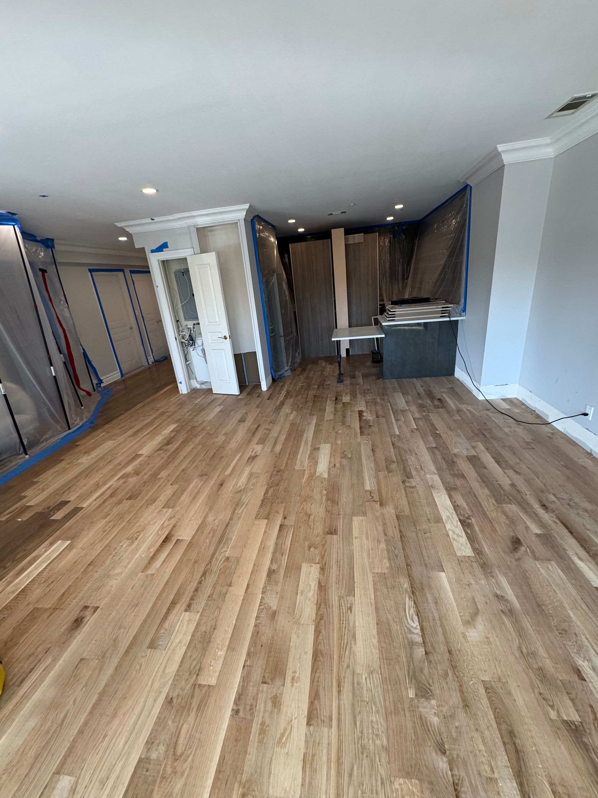Empty apartment interior with wood floors, white walls, and a small kitchen area in the back.