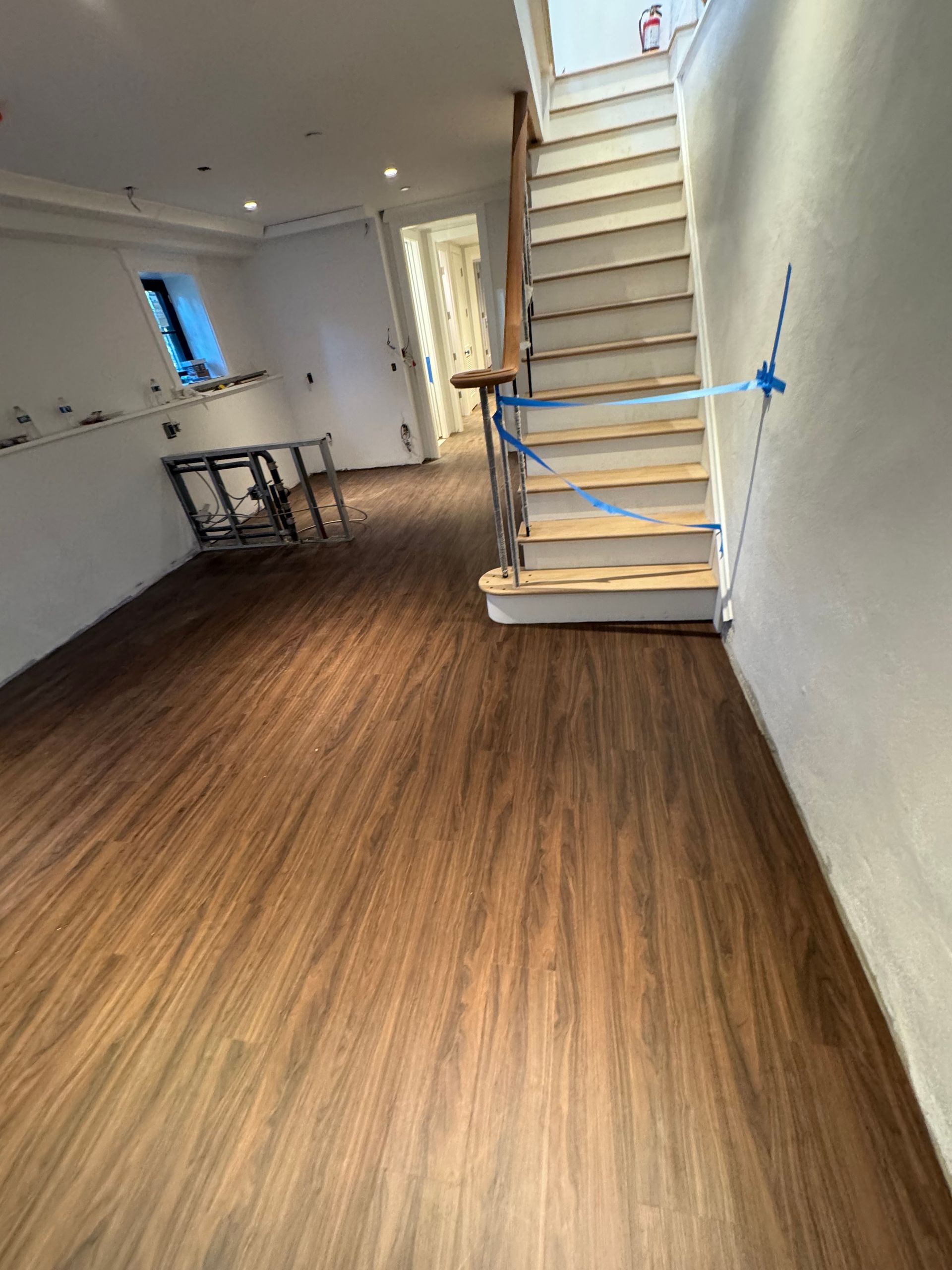 Empty room with wood floors, white walls, and a staircase with blue tape markers.