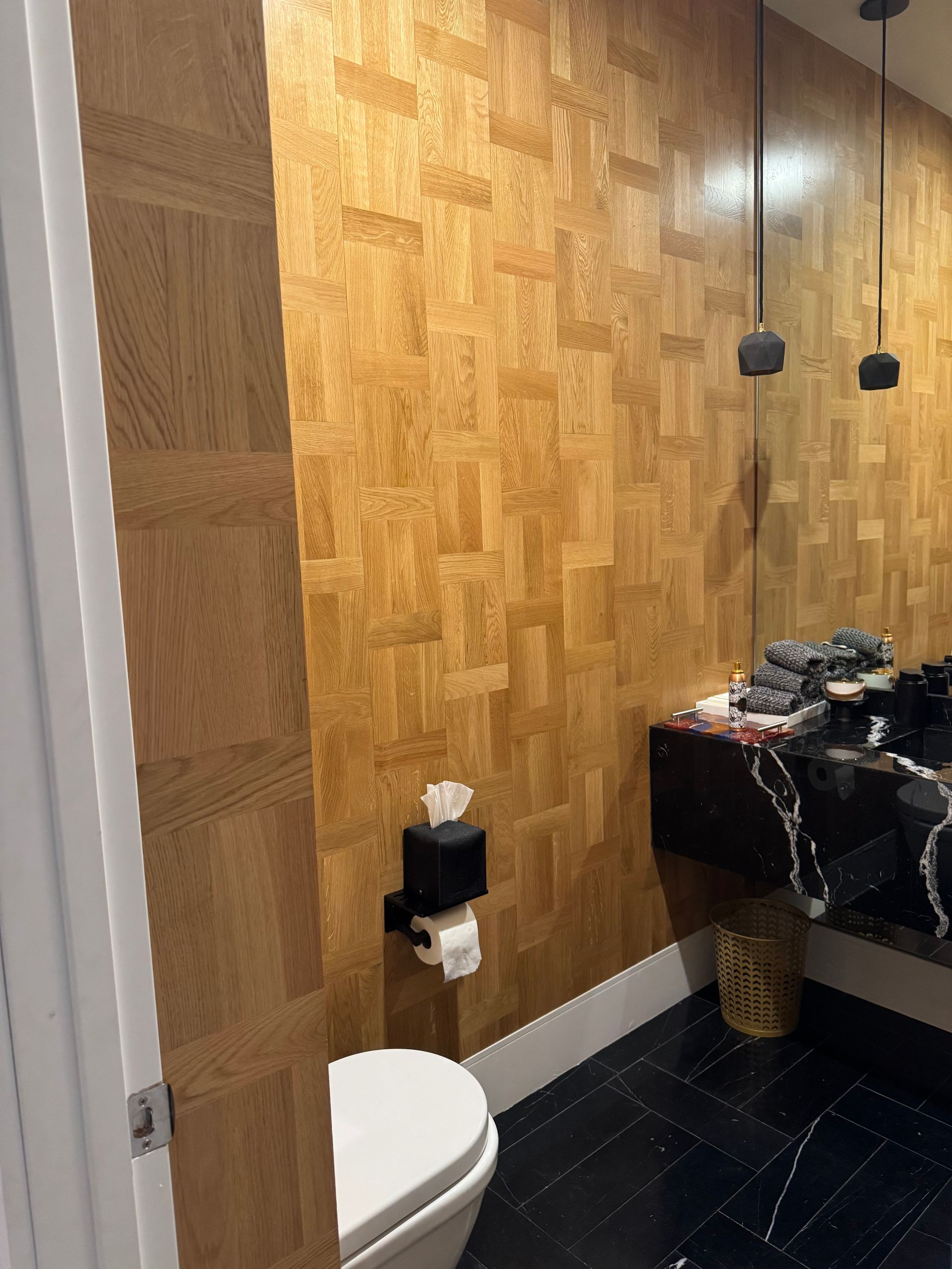 Modern bathroom with wood-paneled walls, black marble vanity, and a visible toilet.
