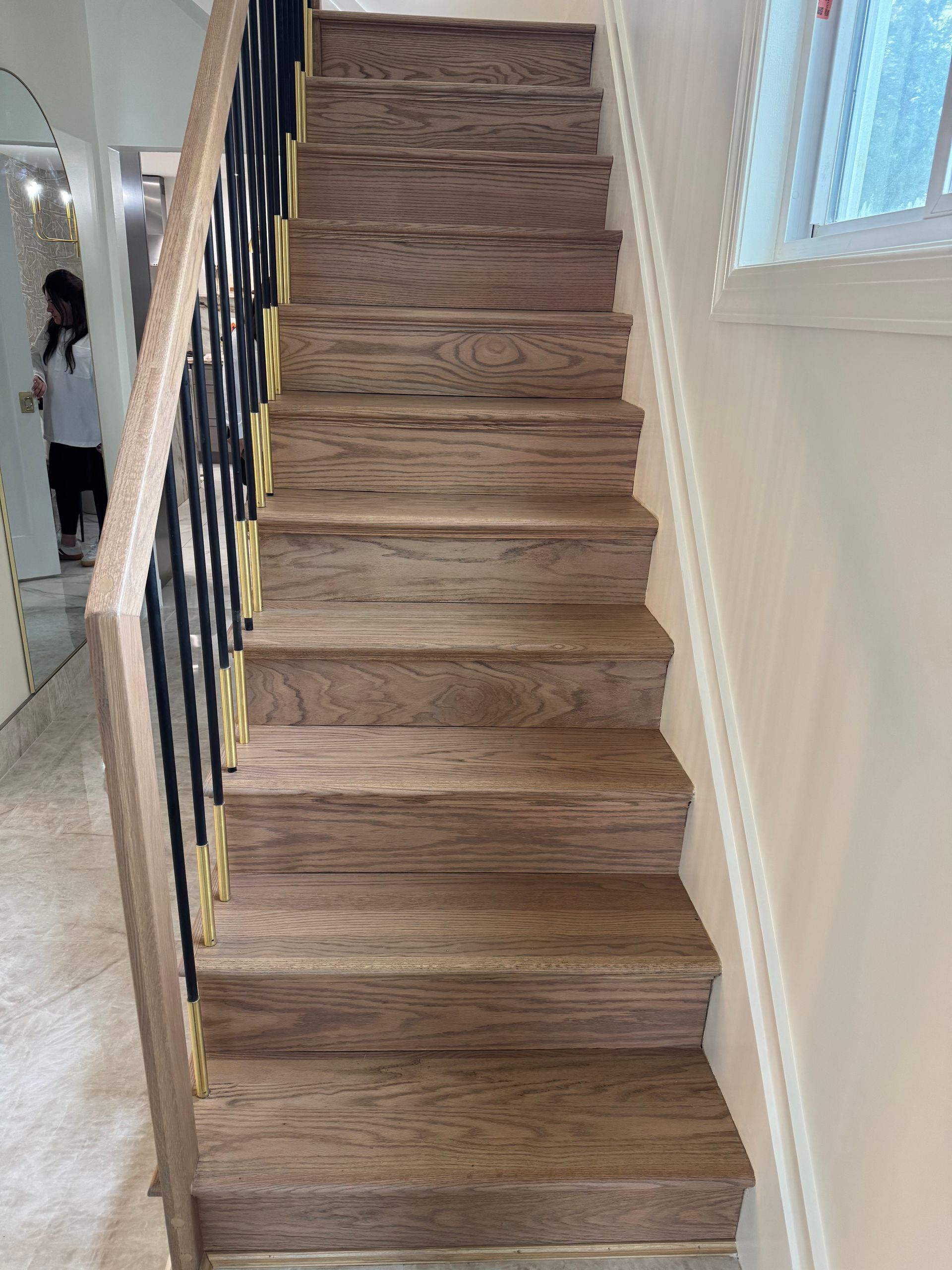 Staircase with wood-look treads and black railings in a bright hallway