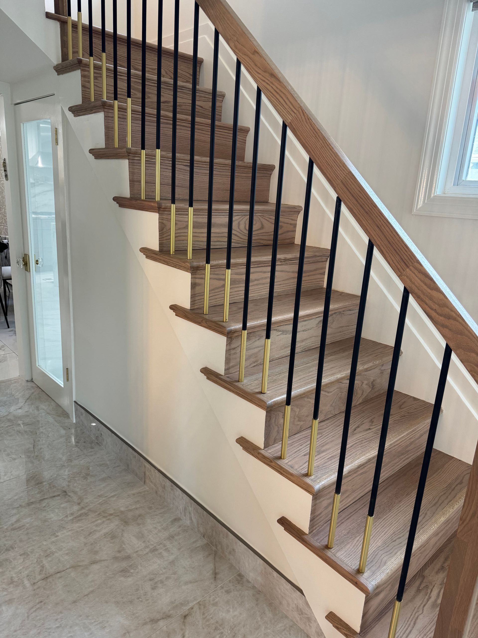 Indoor staircase with carpeted steps, wooden handrail, and black balusters beside a bright hallway.